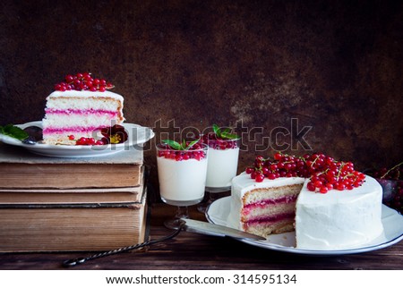 Cakes with red currant decorated with fresh red berries, cream desserts with berries and old books on dark wooden background