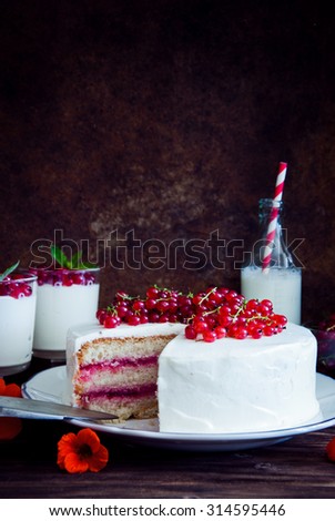 Cakes with red currant decorated with fresh red berries and flowers, cream desserts with berries, milk and old books on dark wooden background