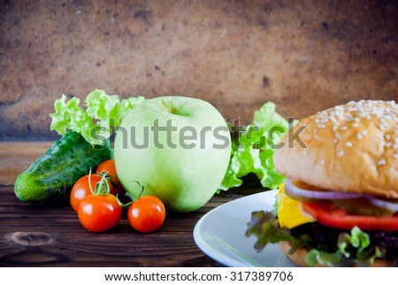 Homemade burger made from fresh vegetables and beef versus fresh fruit and vegetables on wooden background. Healthy and unhealthy food.