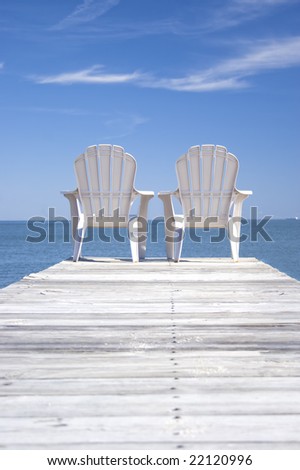 Two chairs sitting at the end of a dock.