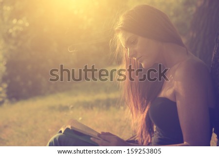 Vintage photo of young woman reading a book in park