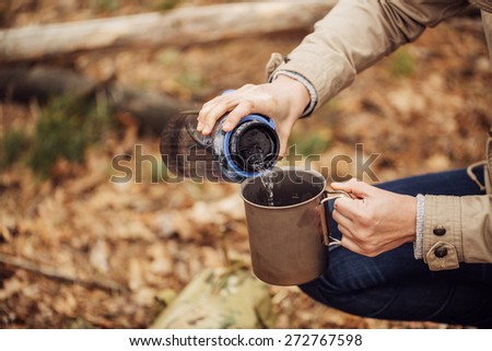 woman pours water from a bottle into a metal mug
