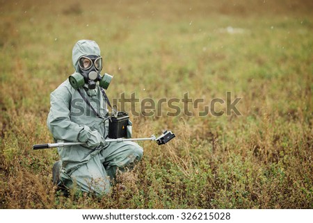 Scientist dosimetrist (radiation supervisor) in protective clothing and gas mask with geiger counter checks the level of radioactive radiation in the danger zone