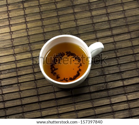 tea cup and tea leaves on a bamboo mat