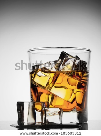 Glass of whiskey with ice melted on gradient background