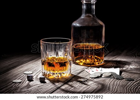 Glass and  bottle of whiskey and playing cards and money on wooden table