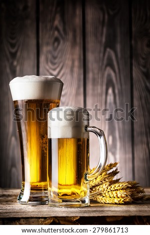 Glass and a mug of light beer with foam and ears on the wooden background