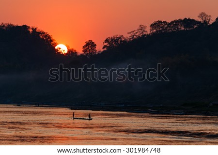 Sunset over mountain and river with boat in silhouette