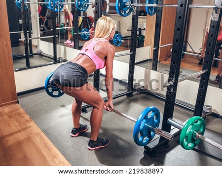 Young sexy woman in the gym doing squat with barbell