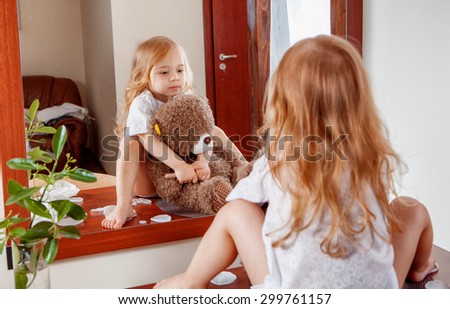 Portrait of little girl with teddy bear looking through near mirror