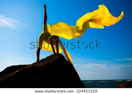 Silhouette of the sports girl with yellow fabric against the sky