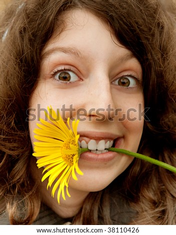 Portrait of the cheerful girl with the big yellow flower in a teeth