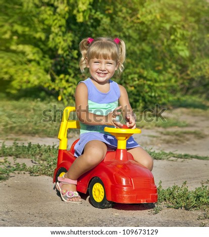 child girl driving her red toy vehicle in the park, outdoors