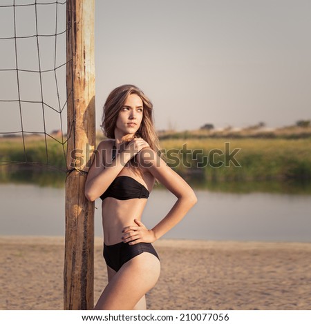 Young beautiful pretty slim sexy girl brunette with long  hair in bikini on sandy beach near volleyball net, outdoors. Summertime. Relaxing on coast. Lifestyle