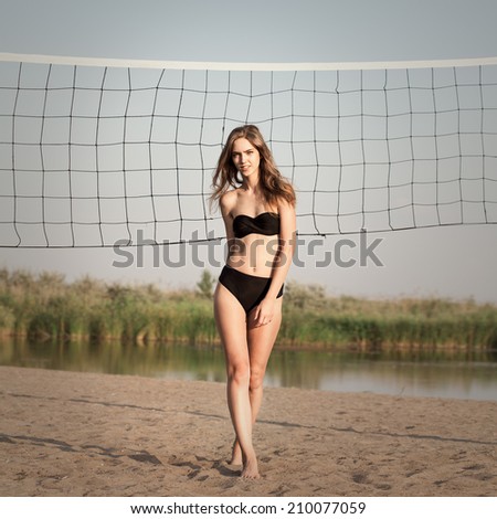 Young beautiful pretty slim sexy girl brunette with long  hair in bikini on sandy beach near volleyball net, outdoors. Summertime. Relaxing on coast. Lifestyle