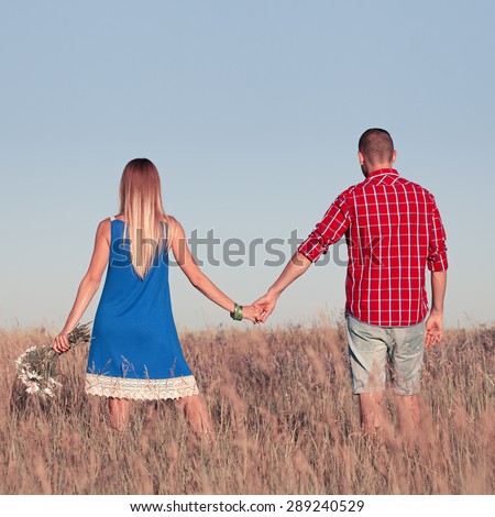 Love story. Beautiful young couple walking in meadow, outdoor. Portrait of stylish fashion man and woman posing in summer in field. Series. Back view