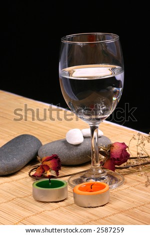 Natural pebbles, candle, glass and dried rose petals on the rattan background. Suitable for spa, relaxation and romance setting