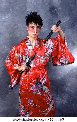 A man dressed as a Geisha, holding nunchaku in a fighting stance
