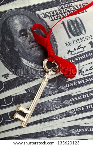 Golden skeleton key on a red cord with a bow on a dollar background/Money key
