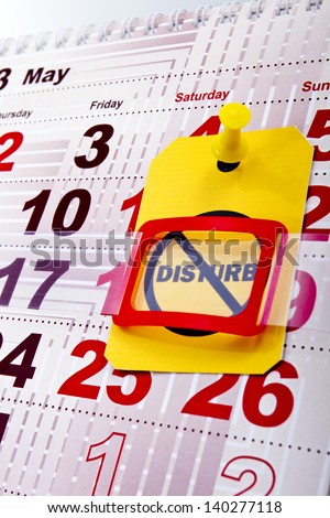 Do not disturb at weekend concept shot. Do not disturb yellow label/tag on a paper calendar background.