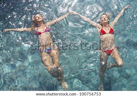 Over head view of two young women wearing bikinis and floating in water while holding hands, full frame.