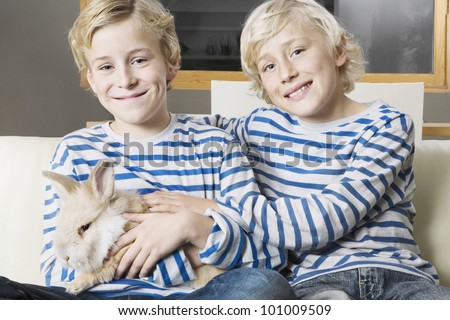Two twin brothers stroking their pet rabbit on a sofa at home.