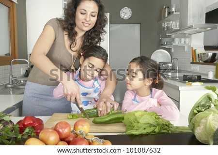 Young mum chopping vegetables with twin daughters in a family home kitchen.
