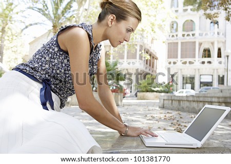 Young businesswoman sitting down and leaning to reach her laptop computer in the city.