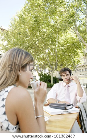 Two business people having a meeting in an outdoors cafeteria in the city and making a phone call.