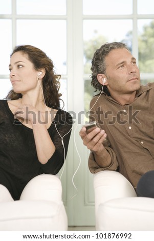 Mature couple sharing earphones while listening to music with an mp4 in their home\'s living room.