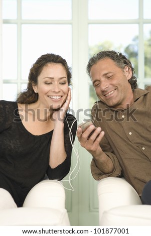 Mature couple sharing earphones while listening to music with an mp4 in their home\'s living room.
