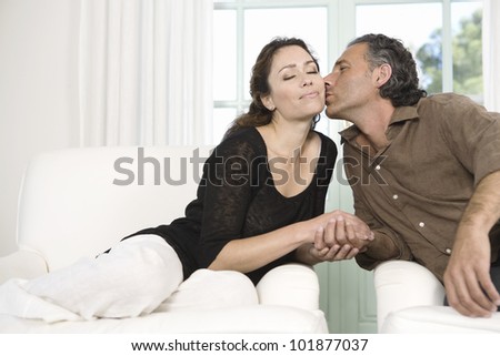 Mature couple kissing while sitting by large garden doors in living room.