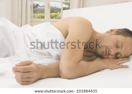 Attractive young man sleeping in a white linen bed.