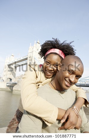 Young african american couple at London's Tower Bridge, hugging and smiling at camera.