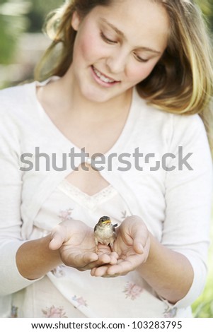 Portrait of a girl in the garden, holding a bird in her hands and smiling.