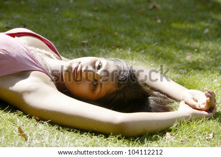 Young indian woman laying down on green grass in the park, smiling.