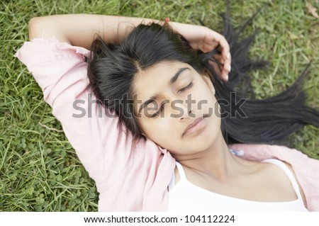 Over head view of an indian girl laying down on green grass with her eyes closed.