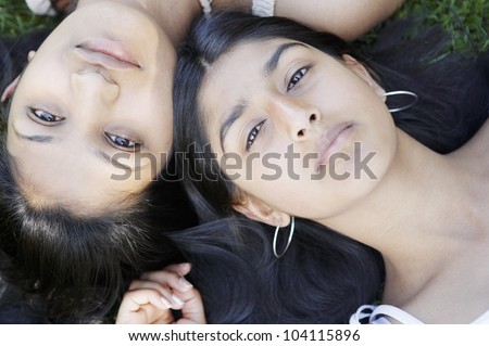 Over head view of two indian girls laying down on grass with their heads together.