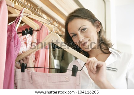 Close up of a store assistant sorting clothes on store\'s rails, smiling.