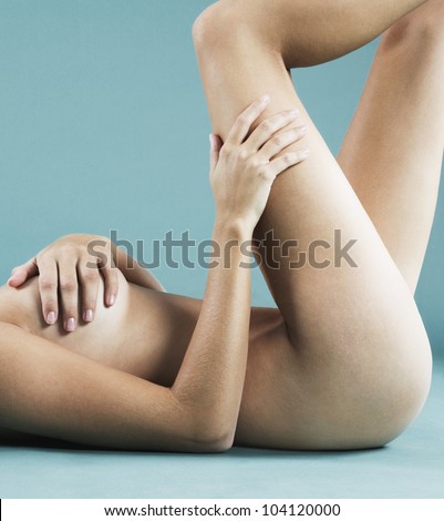Mid body section of a naked tanned woman laying down against a blue background.