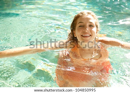 Attractive young woman in a swimming pool in a tropical garden, wearing a pink dress and smiling.