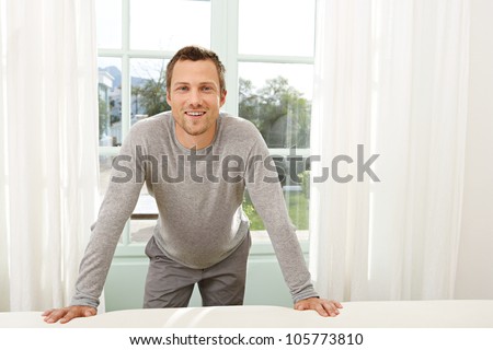 Professional young man leaning on the back of a white sofa at home while standing by a large garden door.