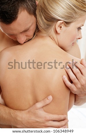 Back view of a man hugging a nude woman at home.
