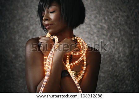 Portrait of a young black woman with Christmas lights around her body, smiling with her eyes closed.