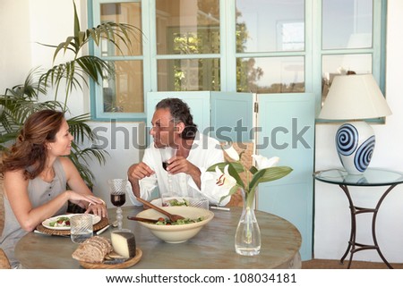 Mature couple eating and drinking together at garden table, while having a lively conversation.