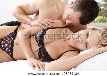 Romantic couple in bed, with man kissing woman\'s shoulder.