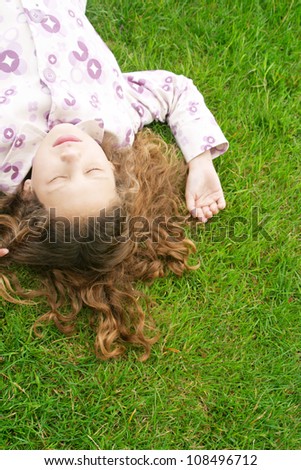 Over head view of a young girl laying down on green grass with her eyes shut.