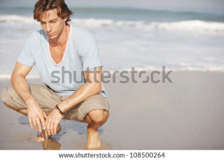 Young attractive man crouching by sea shore on a sunny day.