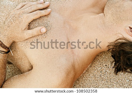 Close up body part detail of a man sunbathing on a golden sand beach with sand grains on the skin.