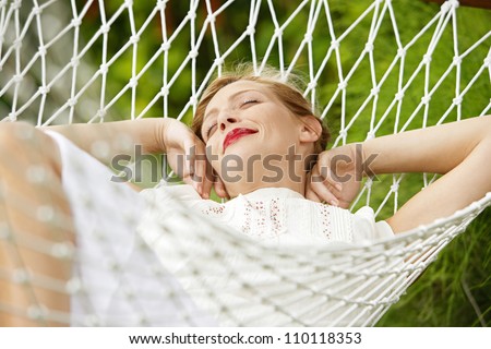 Young attractive woman laying and relaxing on a white hammock in a garden.